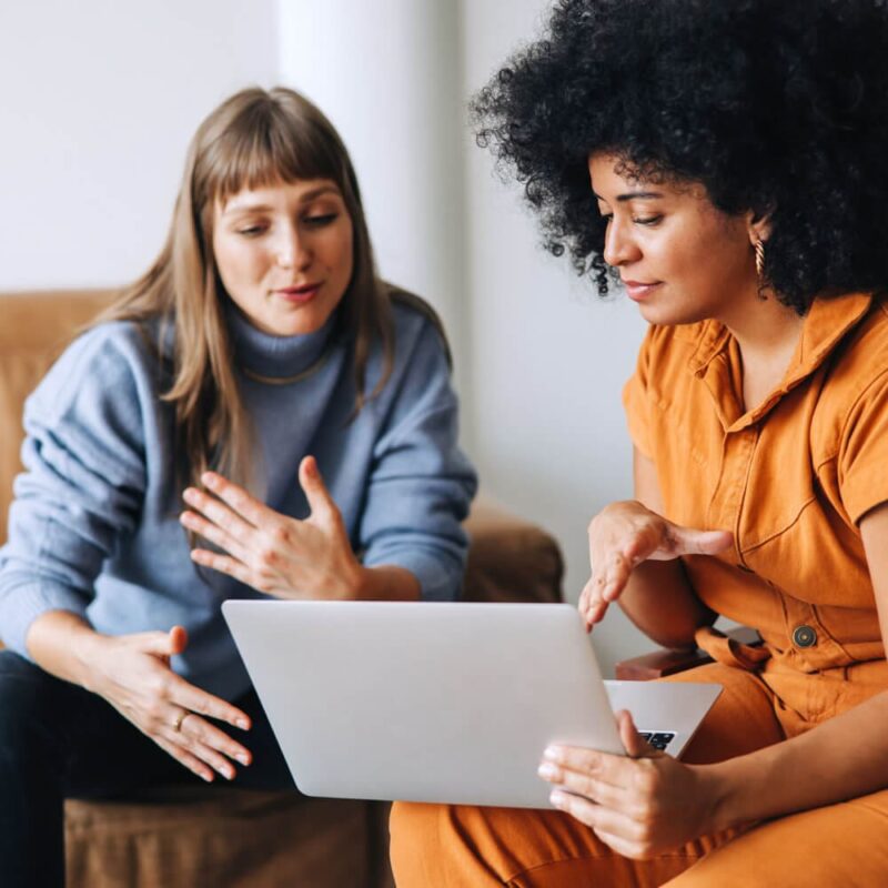 2 women sitting down talking over laptop