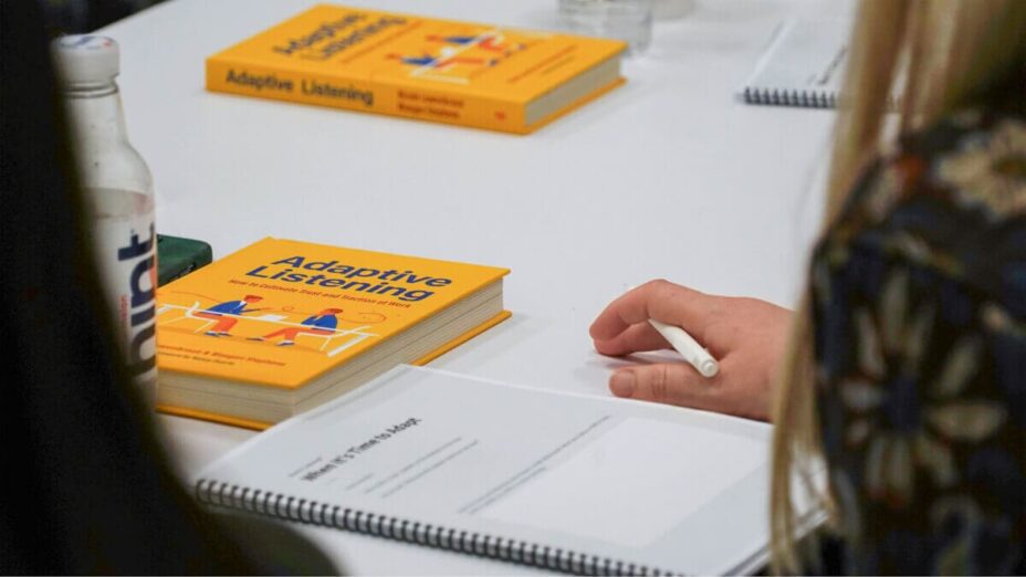A person holding a pen with the Adaptive Listening book and workbook in front of them.