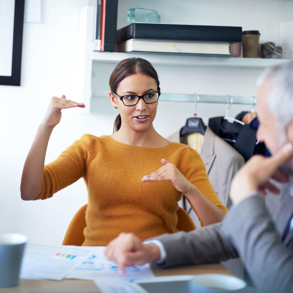 A woman gestures with her hands while talking with someone at a conference table.