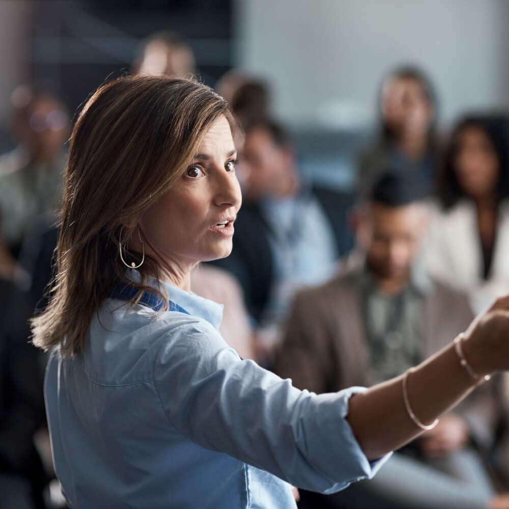 A woman looks behind her while hosting a presentation at a conference.