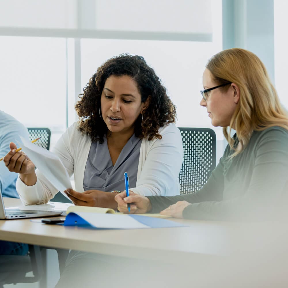 Two women sitting are reviewing a piece of paper.