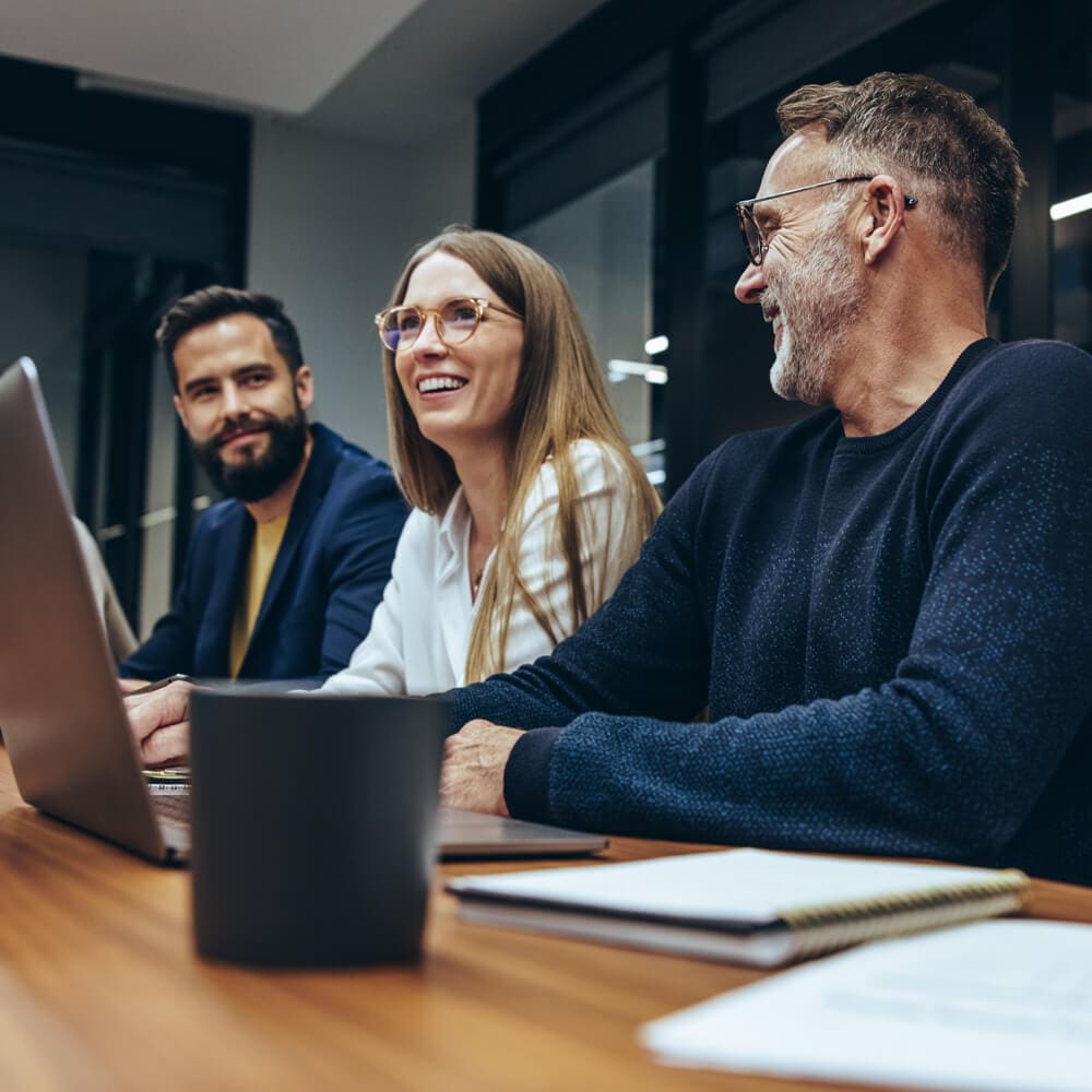 A group of people with laptops smiling and communicating in a conference room.