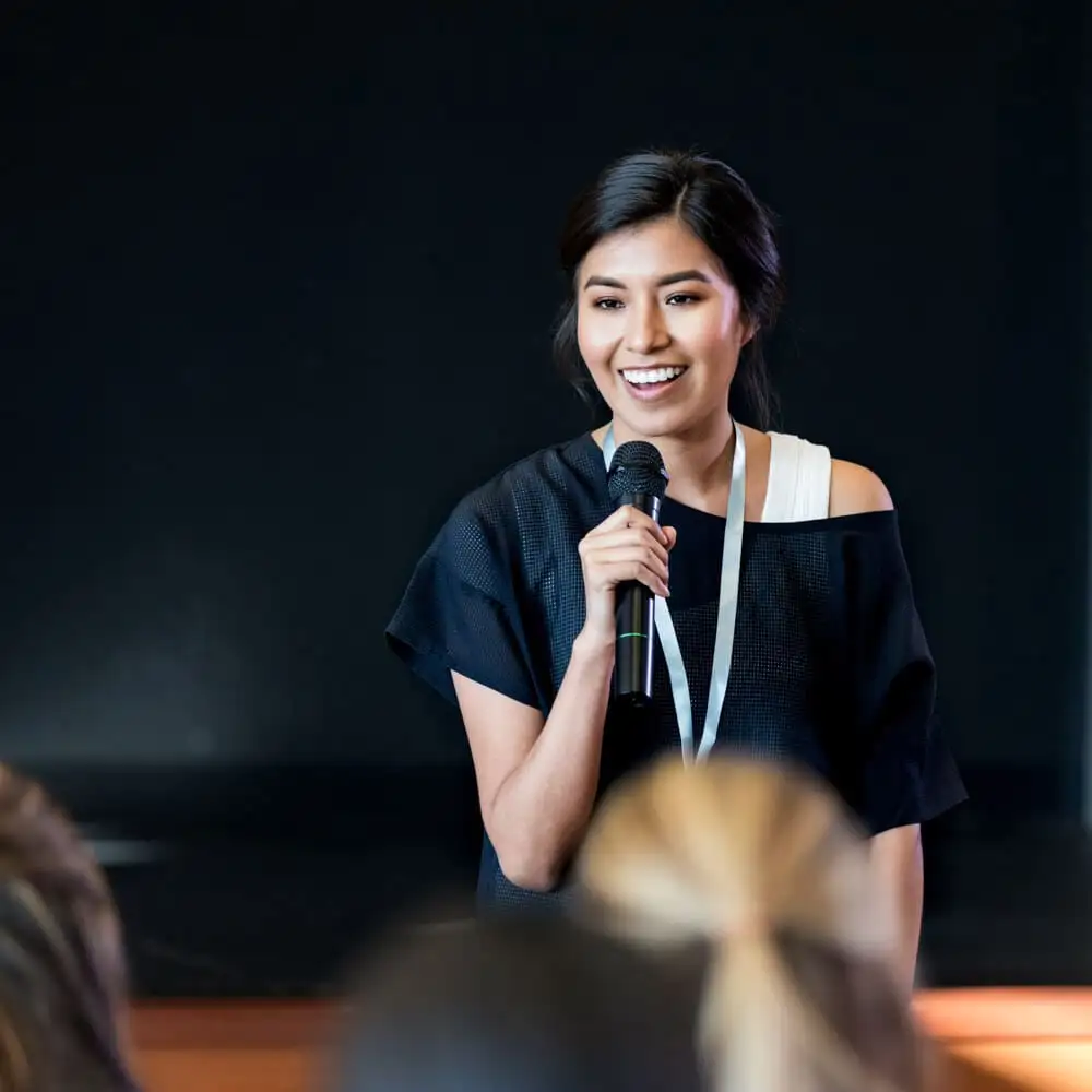 A woman smile while holding a microphone and answering questions at a conference.