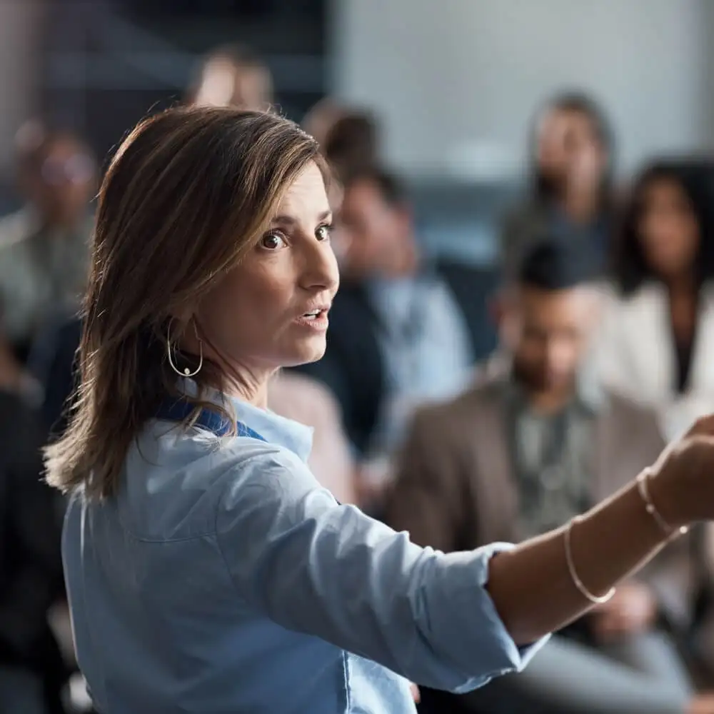 A woman looks behind her while hosting a presentation at a conference.