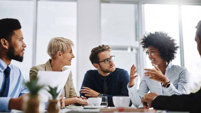 Image of professionals sitting around a conference table where one is giving a presentation with the hope of convincing stakeholders to adopt their idea.