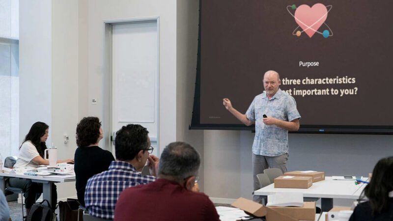 A top-rated Duarte facilitator conducting an in-person Captivate training workshop. The facilitator is standing in front of screen featuring the words “Purpose: What three characteristics are most important to you?” while a group of workshop attendees are facing front with rapt attention.
