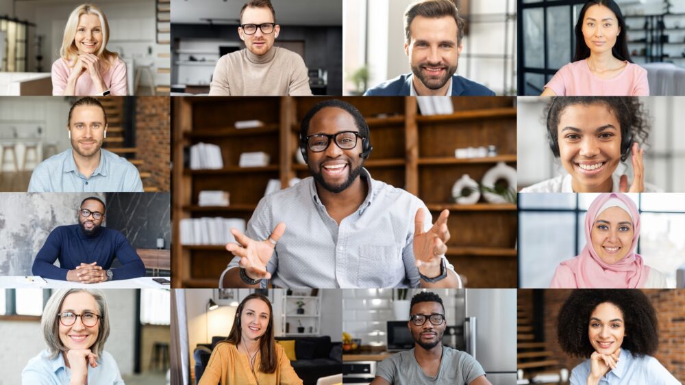 Grid of sixteen diverse professionals smiling at the camera during a video call, with a man in the center wearing headphones and gesturing while speaking.