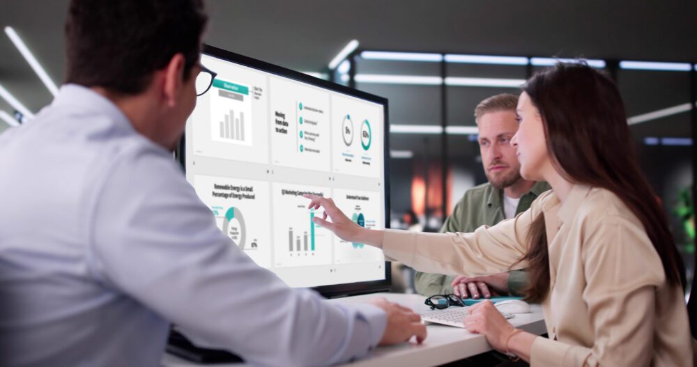 A team reviews a data presentation on a large screen while a presenter points to a chart slide
